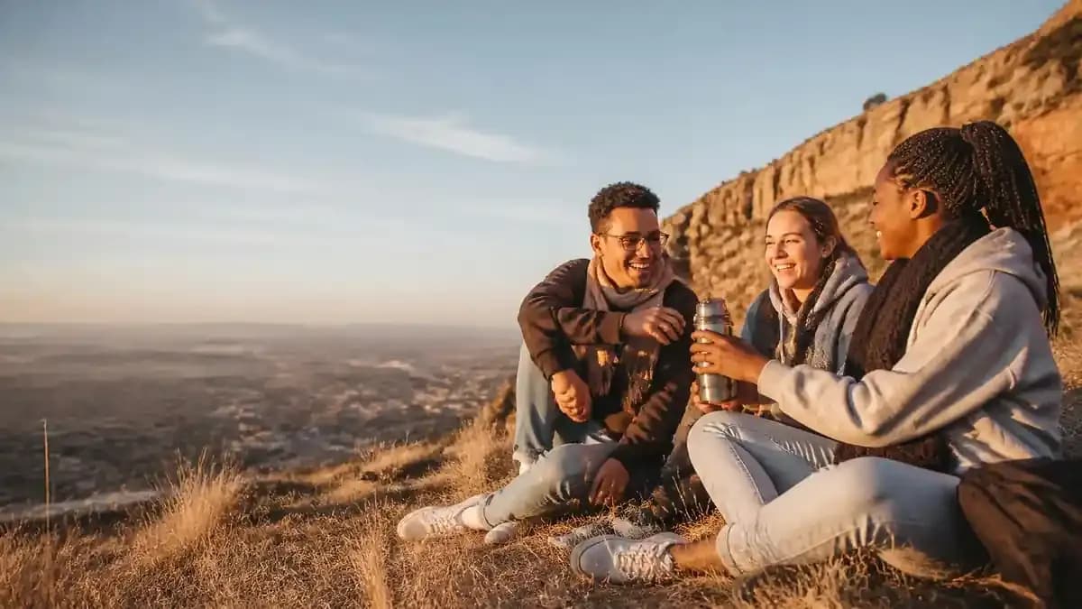 Students sharing coffee on a hilltop at sunset overlooking a flat Highveld city, with sandstone mountains in the distance