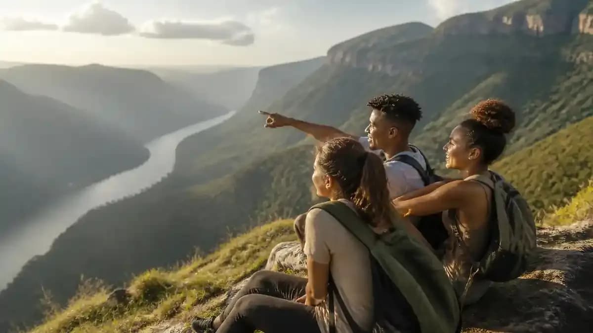 Three students sitting on a rocky edge above a deep green canyon with misty mountains in Mpumalanga